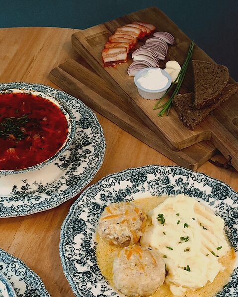 Plato de borsch en loza azul con crema agria, junto a pan negro y salo