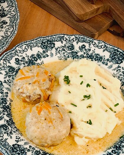 Dos albóndigas en salsa cremosa con puré de patatas, en un plato de loza azul
