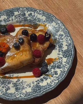 Torrija con arándanos, frambuesas y sirope en un plato de loza azul