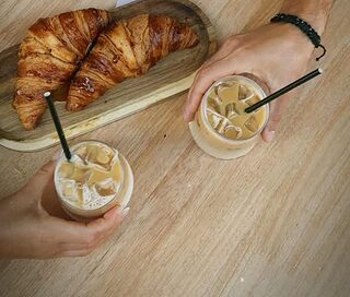 Dos manos con cafés con hielo junto a croissants sobre la mesa