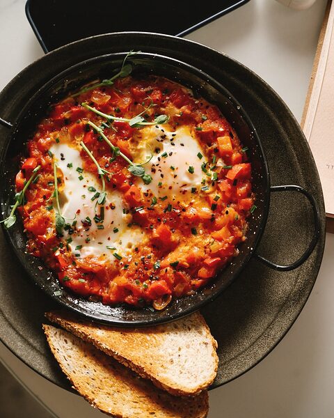 Shakshuka en sartén de hierro con huevos, tomate y rebanadas de pan tostado
